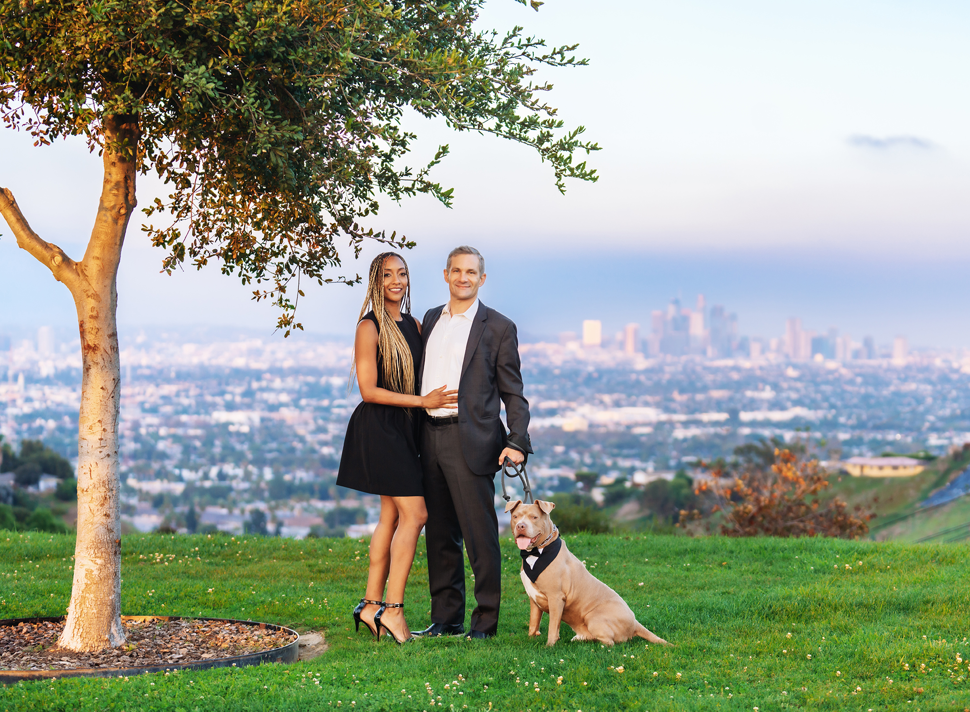 A couple dressed in formal attire with their dog taking engagement photos in Los Angeles with a view of downtown L.A. with Emily Winnie Photography.