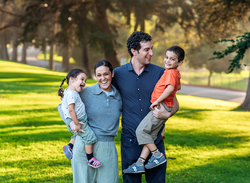 A happy family laughing and playing together in a sun-drenched Los Angeles park during a summer sunset session.